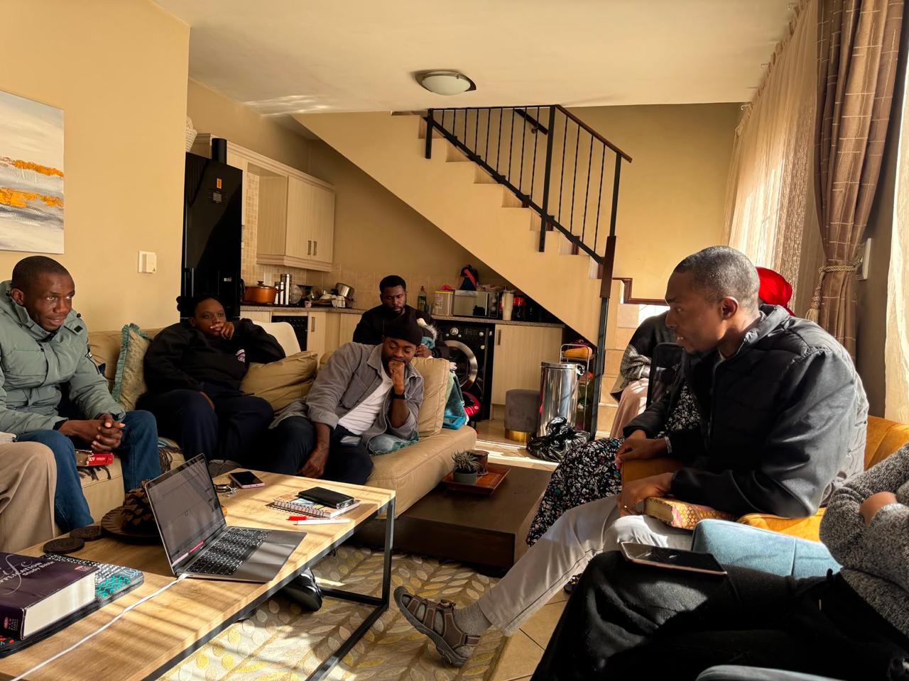 Brothers gathered on the couches around a laptop during a home fellowship